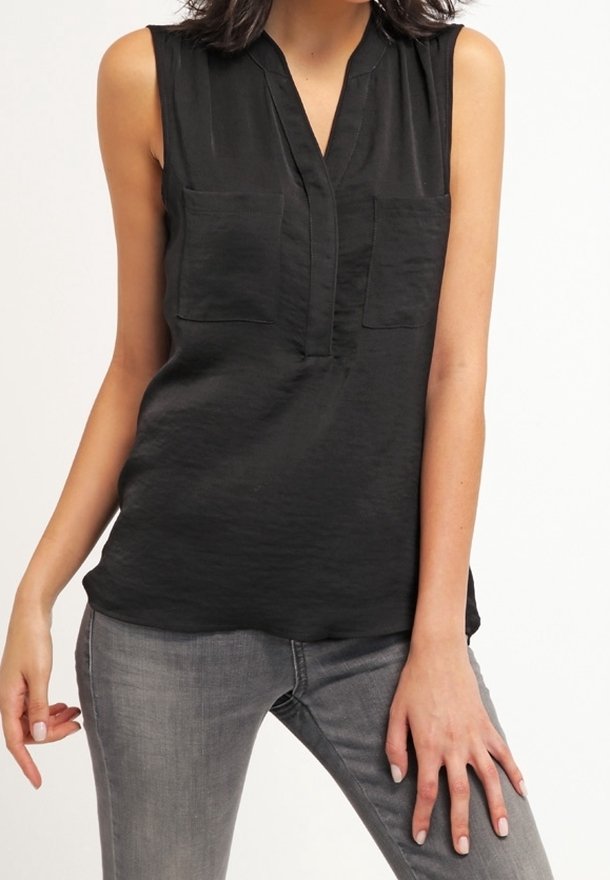 Top negro sin mangas con escote en V, dos bolsillos delanteros, textura suave y un corte relajado, combinado con jeans de mezclilla grises.