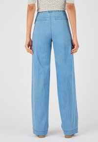 Pantalones de mezclilla de pierna ancha en azul claro con cintura alta, dos bolsillos traseros y dobladillos enrollados. Textura suave con detalles de costura sutiles.