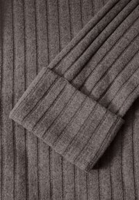 Texturierter, gerippter Stoff in einer gedämpften braunen Farbe. Verfügt über einen breiten Bund mit einem weichen, dicken Griff, der das vertikale Streifenmuster hervorhebt.