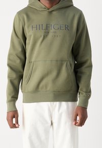 Felpa verde oliva in misto cotone, con tasca a marsupio frontale, cappuccio con cordino e logo stampato "HILFIGER NEW YORK EST 1985."