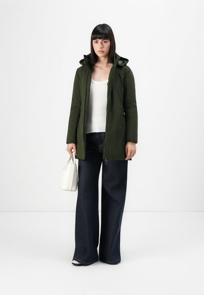 Parka matelassée vert foncé avec capuche, fermeture éclair à l'avant et deux poches latérales, associée à un jean en denim foncé à jambes larges et un petit sac à main blanc.