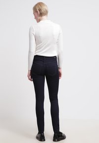 Mørkeblå skinny jeans med middels høy midje og baklommer, kombinert med en hvit ribbestrikket langermet topp.
