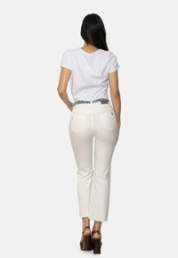Pantalones blancos recortados con un dobladillo deshilachado, combinados con una camiseta blanca sencilla. Un cinturón con patrón añade contraste. Sandalias marrones de tacón grueso completan el look.