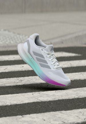 White athletic sneaker with gray stripes and gradient sole hovering above a black and white crosswalk, kicking up small dirt particles.