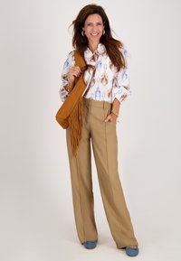 Witte blouse met blauwe en bruine patronen, tan wijde pantalon, bruine franjes tas en blauwe flats. Gouden sieraden accentueren de outfit.