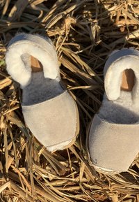 Chaussons en daim beige avec doublure blanche duveteuse et semelle souple, présentant un bout arrondi et des détails de couture minimalistes.