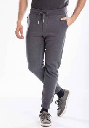 Pantalons de survêtement gris avec une taille à cordon, coupe fuselée et poches latérales, fabriqués dans un tissu doux et texturé. Portés avec des baskets grises.