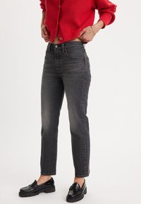 Jeans grises de talle alto con un diseño de pierna recta y textura desgastada. Combinados con un cárdigan de punto rojo brillante y mocasines negros.