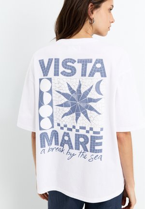Witte katoenen t-shirt met een blauwe grafische ontwerp op de achterkant, met de tekst "VISTA MARE" en een mozaïeksterpatroon. Korte mouwen.