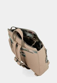 Bolso de mano de cuero beige con asas dobles, compartimento principal con cremallera, encantos metálicos decorativos y forro interior con un patrón floral.