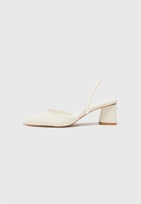 White slingback heeled shoe with a pointed toe, smooth texture, and a block heel. Features a thin strap at the back for secure fit.
