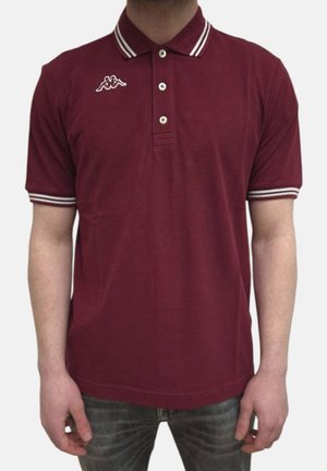 Homme portant un polo bordeaux à manches courtes avec des doubles bandes blanches sur le col et les manches, et un petit logo sur la poitrine gauche.