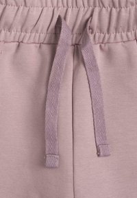 Světlé růžové tepláky s elastickým pasem a nastavitelnými šňůrkami, vyrobené z texturované tkaniny. Měkký materiál bez viditelných vzorů.