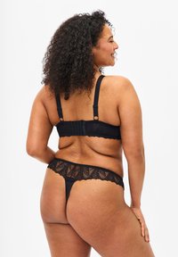 Black lace bra and thong set, featuring adjustable straps, floral lace detailing, and a sheer texture for both pieces.
