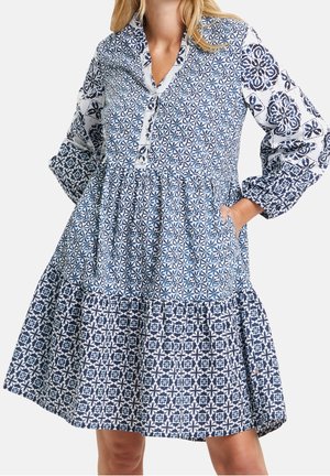 Mujer con un vestido hasta la rodilla con patrones florales geométricos mixtos en azul y blanco y mangas largas abullonadas.