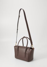 Sac à main en cuir marron avec surface texturée, petites poignées et bandoulière longue amovible. Équipé de quincaillerie dorée et d'une doublure intérieure rouge.