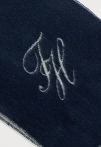 Jūrā zilas vilnas šalle ar mīkstu tekstūru, ar baltu izšūtu monogrammu un kārtīgi apstrādātām malām.