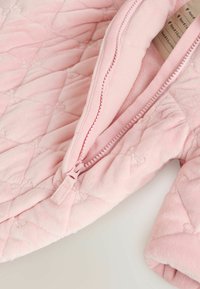 Veste en polaire rose matelassée avec une texture douce, dotée d'une fermeture éclair et d'un col arrondi. Agrémentée d'un motif de couture en losanges.
