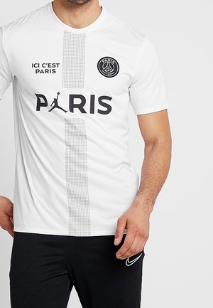 Biała sportowa koszulka z napisem "ICI C'EST PARIS", pionową kropkowaną linią, logo Paris Saint-Germain oraz napisem "PARIS", gdzie litera A została zastąpiona logo Jordan Jumpman.