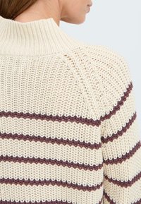 Strickpullover mit hohem Rippenkragen, in Cremefarbe mit burgunderroten horizontalen Streifen. Strukturstoff mit lockerer Webart.