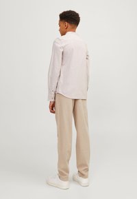Ljusbeige långärmad skjorta med knappränder och en rundad nederkant, ihopparad med lös passform beiga byxor och vita sneakers.