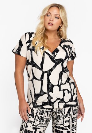 Korte mouw top in crème met gedurfde zwarte abstracte patronen, V-hals ontwerp en zachte textuur. Gecombineerd met bijpassende geblokte broek.