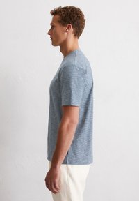 Hellblaue Kurzarm-T-Shirt mit strukturiertem, meliertem Muster. Rundhalsausschnitt und eine bequeme Passform, kombiniert mit hellen Hosen.