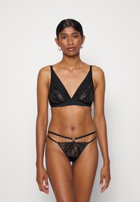 Svart underkläder set som har en triangulär bralette med spetsdetaljer och en matchande tanga med ett geometriskt spetsmönster och band.