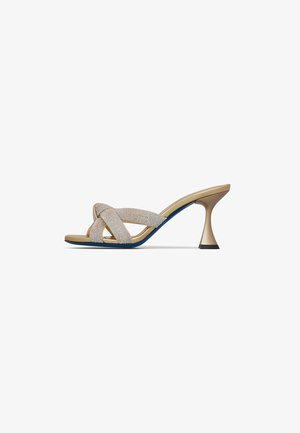 Sandalo mule beige con tacco alto, con cinturini incrociati texturizzati e tacco svasato scolpito su sfondo bianco semplice.