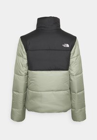 Padded jacket z czarną górną częścią i jasnoskalnym dołem. Posiada wysoki kołnierz i logo z tyłu. Gładka tekstura, ocieplana konstrukcja.