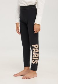 Leggings neri con una cintura metallica elasticizzata. "PARIGI" in paillettes sulla gamba sinistra, caratterizzati da una trama di tessuto liscia e un design aderente.