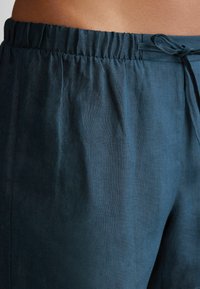 Mörk teal linnebyxor med elastisk midja, dragsnöre och slät yta. Har en avslappnad passform och en subtil glans.