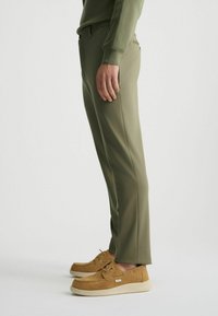 Pantalones a medida verde oliva con un diseño de corte ajustado, que presentan una textura suave, bolsillos laterales y combinados con zapatos de ante marrón claro.