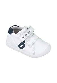 Zapato de cuero blanco con acentos en azul marino, dos tiras de Velcro, punta redondeada y suela de goma texturizada. Presenta un logo en el costado.