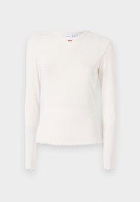 Långärmad, ribbad vit topp med rund halsringning, fransad nederkant och subtil blomsterdetalj nära kragen. Mjuk, strukturerad tyg.