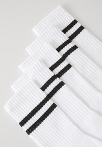 Chaussettes en coton blanches avec une texture côtelée, présentant deux rayures horizontales noires autour du mollet. Quatre paires disposées en pile.