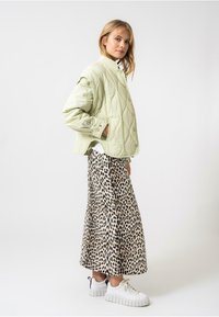 Ljusgrön vadderad jacka med hög krage, över en lång leopardmönstrad kjol. Vita klumpiga sneakers kompletterar looken.