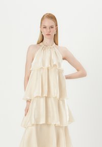 Layered halter top in cream satin with a ruffled design. Features a gathered neckline and flowing silhouette. Smooth, shiny texture.
