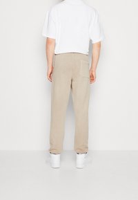 Beige sweatpants med rak passform och bakficka. Modellen bär en vit t-shirt och vita sneakers, vilket ger en avslappnadstil.