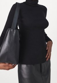 Person som bär en svart ribbad tubhalsduk, svart läderkjol och bär en stor svart läderaxelväska på vänster axel.