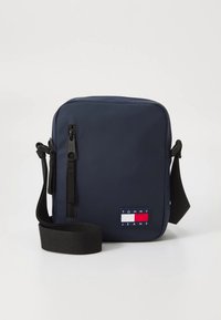 Navy blue rectangular crossbody bag in water-resistant fabric. Features a zippered front pocket and a logo patch with red, white, and blue accents.