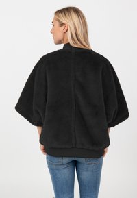 Czarny płaszcz z sztucznego futra w oversize'owym fasonie z krótkimi rękawami i wysokim kołnierzem. Posiada ribbowany dół oraz gładką teksturę. Prosty, nowoczesny design.