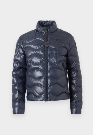 Navyblå quiltet dunjakke med høy krage, glidelås foran, sidelommer og en liten svart hjerteformet merkelapp på brystet.