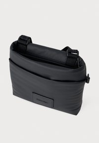 Crna najlonska torba za crossbody s teksturiranom površinom, gornjim poklopcem i podesivim trakama. Sadrži logotip od kože na prednjoj strani.