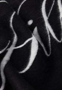 Tissu en laine noir avec une texture douce, présentant un motif abstrait blanc. Le design se détache nettement sur le fond noir.