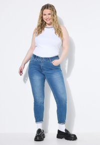 Lehký bílý top bez rukávů spárovaný s fitted modrými džíny. Džíny mají vysoký pas a délku do kotníků, s mírným vyblednutím. Černé platformové boty.