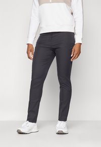 Šauri tumši pelēki bikses, izgatavotas no gludas auduma, ar platu priekšpusi un nelielu stiept, apvienotas ar baltām sporta apavām.