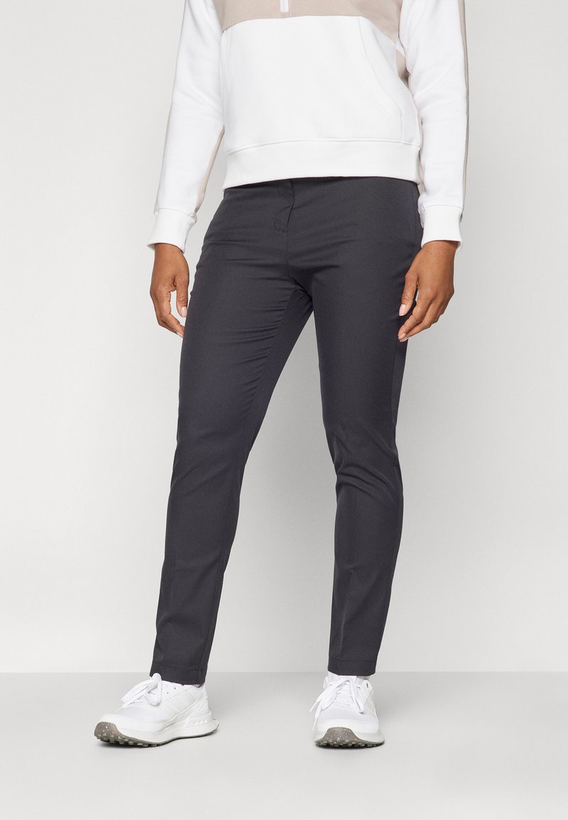 Šauri tumši pelēki bikses, izgatavotas no gludas auduma, ar platu priekšpusi un nelielu stiept, apvienotas ar baltām sporta apavām.