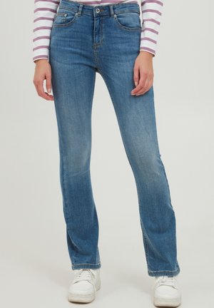 Blaue Denim-Jeans mit geradem Schnitt, Fünf-Taschen-Design, subtilen Verblassungen und standardmäßiger Taille. Kombiniert mit weißen Sneakern.