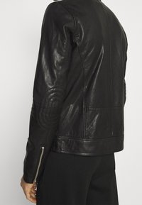 Černá kožená bunda pro motocyklisty s přiléhavým střihem, žebrovanými detaily na ramenou a zipy na manžetách. Hladká textura s jemným leskem.